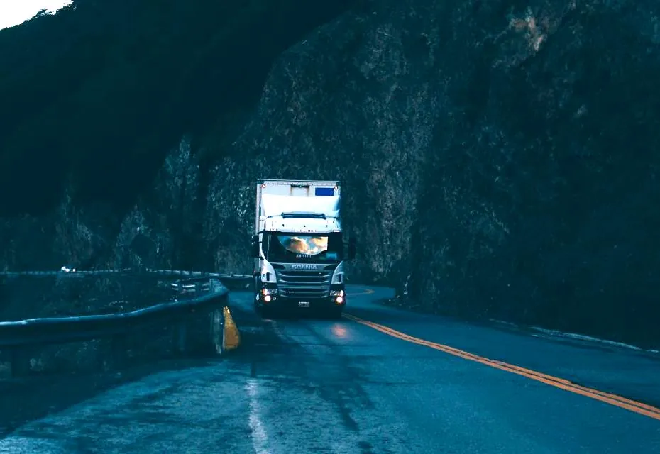 Poids lourd en approche sur une route de transit, phares allumés.